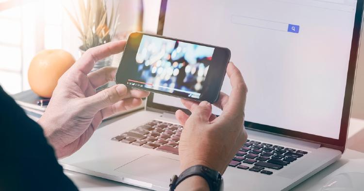 A person watching a video on their phone, while they have their laptop open